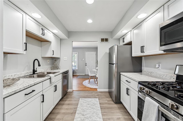 kitchen featuring appliances with stainless steel finishes, sink, light wood-type flooring, white cabinetry, and light stone counters