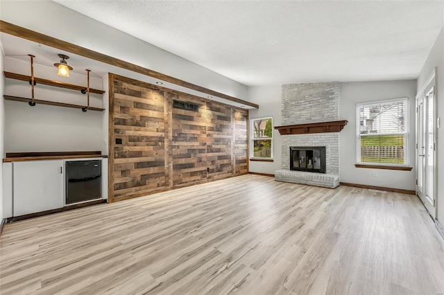 unfurnished living room with wood walls, light wood-type flooring, lofted ceiling, and a brick fireplace