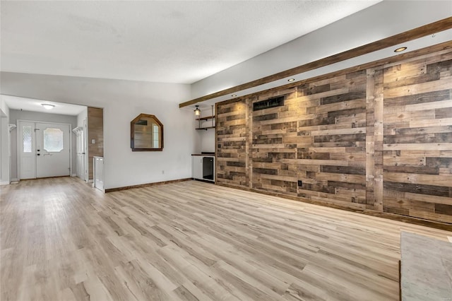 unfurnished living room with a textured ceiling, light wood-type flooring, vaulted ceiling, and wooden walls