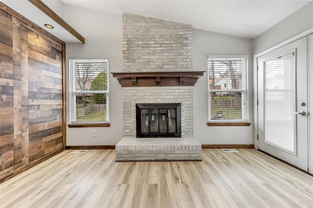 unfurnished living room featuring wood walls, lofted ceiling, light hardwood / wood-style flooring, a textured ceiling, and a fireplace