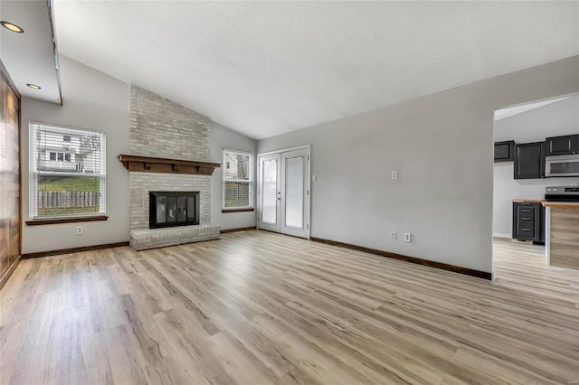 unfurnished living room with a brick fireplace, high vaulted ceiling, and light wood-type flooring