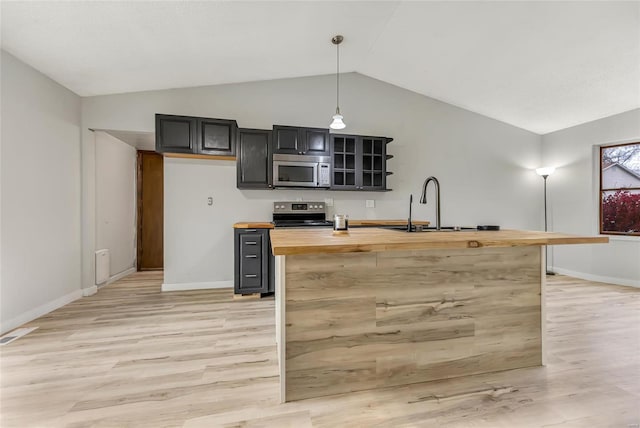 kitchen with stainless steel appliances, wooden counters, lofted ceiling, decorative light fixtures, and a center island with sink