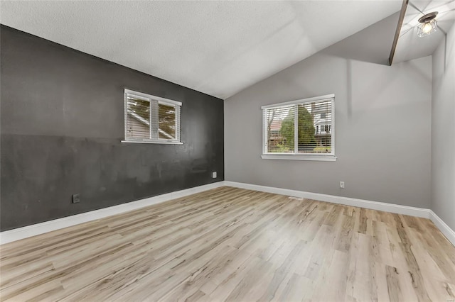 spare room with a textured ceiling, light hardwood / wood-style floors, and vaulted ceiling