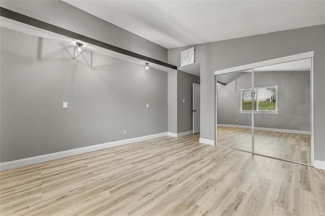 unfurnished bedroom featuring a textured ceiling, light wood-type flooring, vaulted ceiling, and a closet