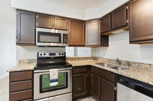 kitchen with appliances with stainless steel finishes, sink, light stone countertops, dark brown cabinets, and a textured ceiling