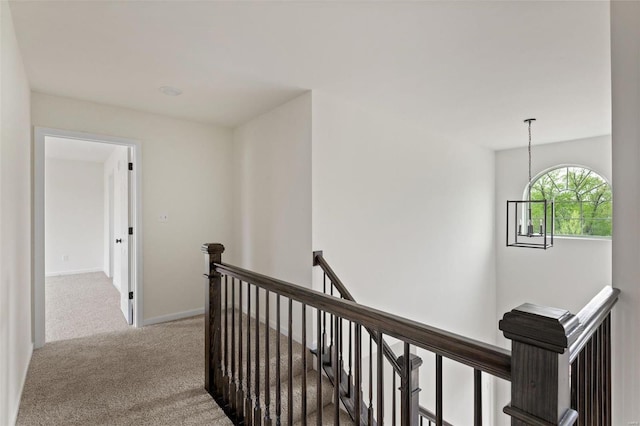 hallway featuring an inviting chandelier and light colored carpet