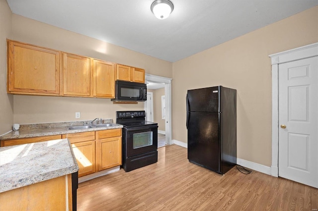 kitchen with light stone counters, black appliances, sink, and light wood-type flooring