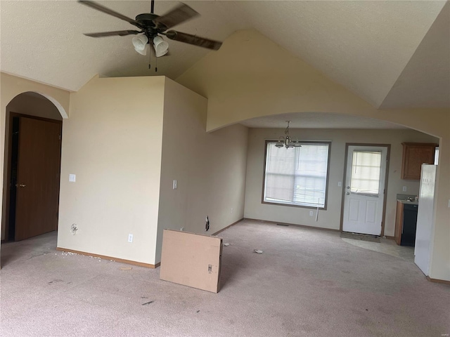 unfurnished living room with light carpet, a textured ceiling, lofted ceiling, and ceiling fan with notable chandelier