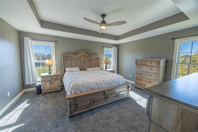 carpeted bedroom with ceiling fan and a raised ceiling