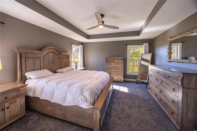 bedroom with ceiling fan, a tray ceiling, and dark carpet