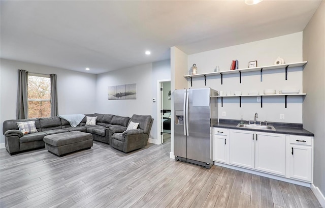 kitchen with stainless steel fridge, white cabinetry, sink, and light wood-type flooring