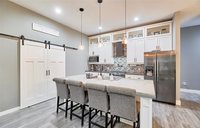 kitchen featuring white cabinets, a barn door, wall chimney range hood, pendant lighting, and appliances with stainless steel finishes