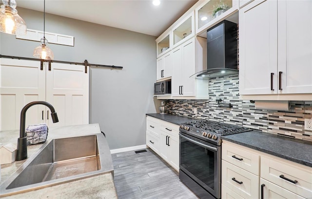 kitchen with gas stove, wall chimney range hood, a barn door, pendant lighting, and sink