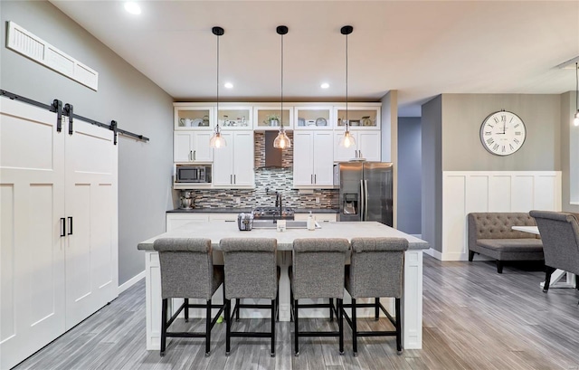 kitchen featuring white cabinets, appliances with stainless steel finishes, a barn door, and hanging light fixtures