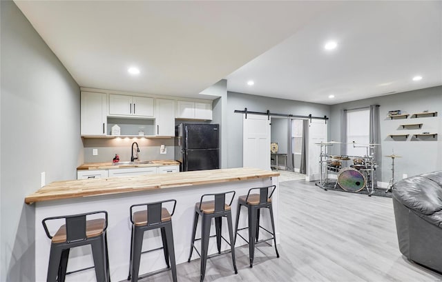 kitchen with black refrigerator, a barn door, a breakfast bar area, sink, and butcher block countertops