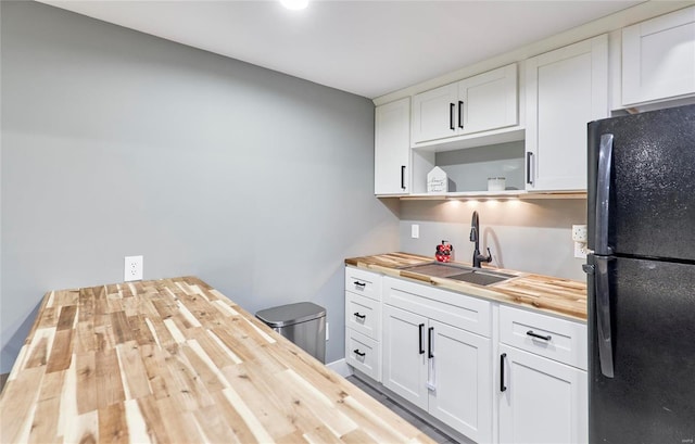 kitchen with white cabinets, wood counters, sink, and black refrigerator