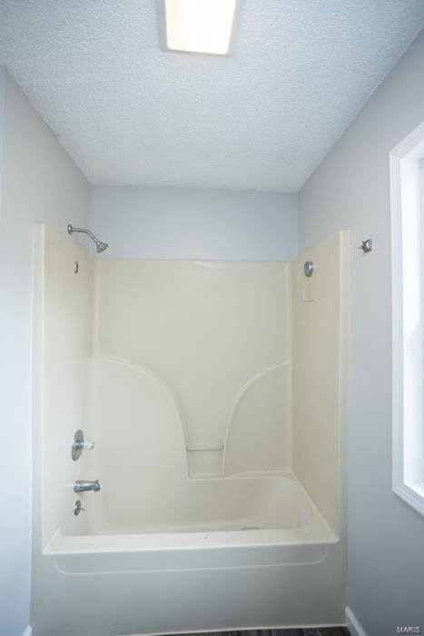 bathroom with a textured ceiling and bathing tub / shower combination