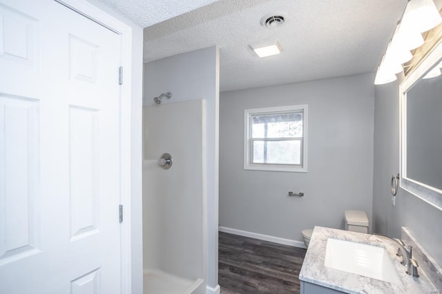 bathroom with a textured ceiling, walk in shower, wood-type flooring, toilet, and vanity