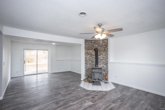 unfurnished living room featuring a wood stove, dark hardwood / wood-style floors, a textured ceiling, and ceiling fan