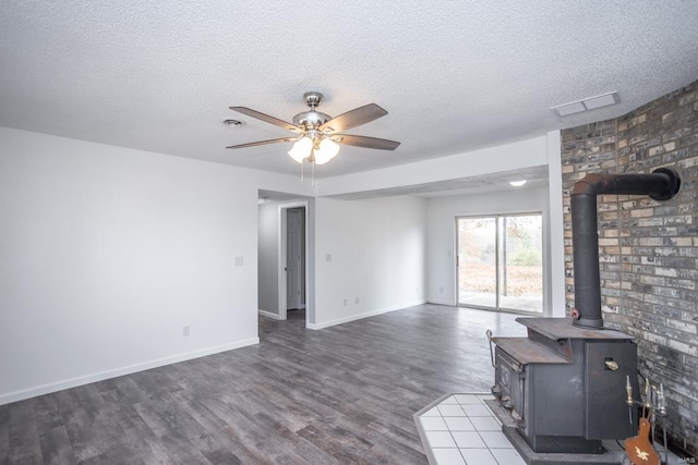 unfurnished living room with ceiling fan, a textured ceiling, a wood stove, and dark hardwood / wood-style flooring