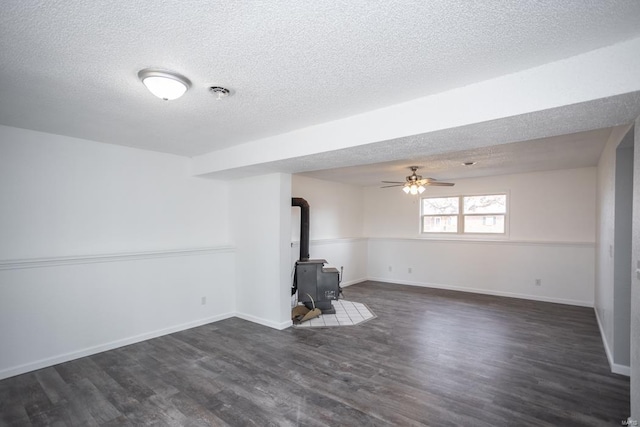 unfurnished living room featuring dark wood-type flooring, a textured ceiling, a wood stove, and ceiling fan