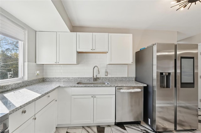 kitchen with white cabinets, appliances with stainless steel finishes, light stone countertops, and sink