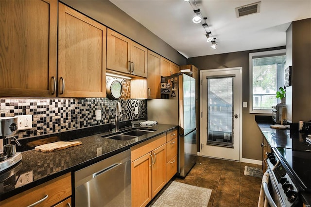 kitchen featuring sink, stainless steel appliances, backsplash, dark stone counters, and track lighting