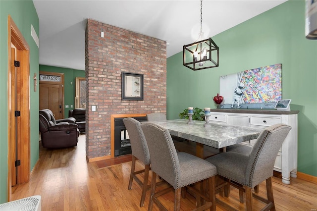 dining space with a chandelier, vaulted ceiling, and light hardwood / wood-style flooring