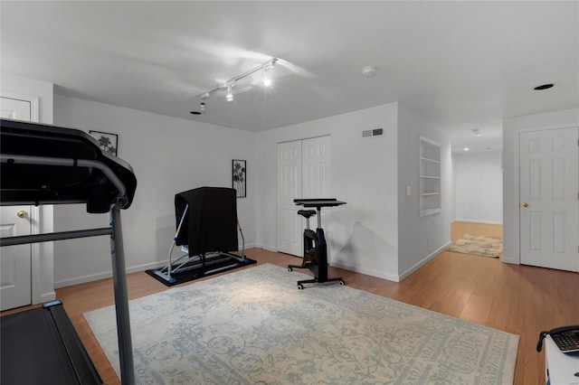 workout area featuring light wood-type flooring, rail lighting, and built in features