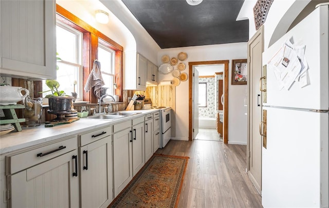 kitchen with light hardwood / wood-style floors, sink, white appliances, and white cabinets