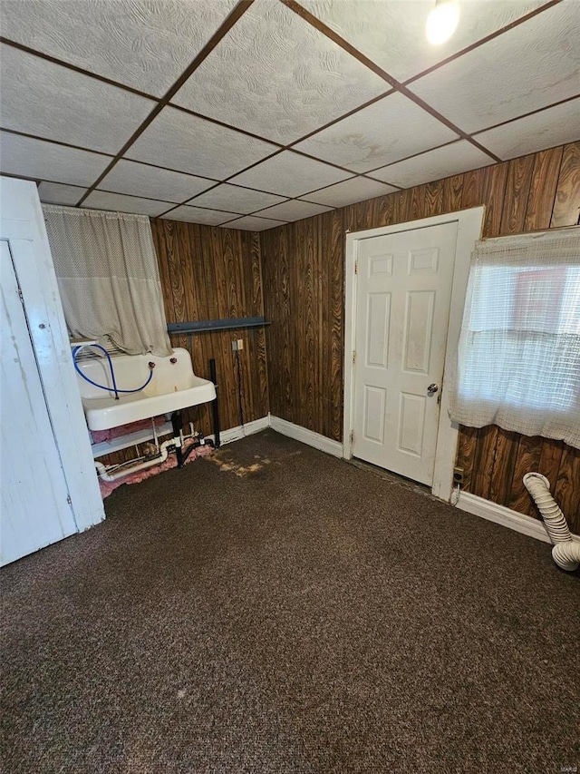 interior space with carpet flooring, a paneled ceiling, and wooden walls