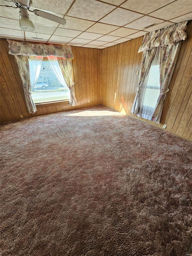 unfurnished room with a paneled ceiling, wooden walls, and carpet