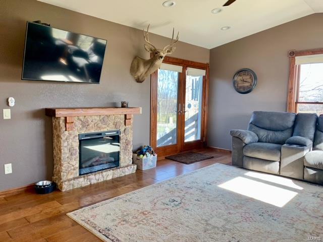 living room featuring french doors, lofted ceiling, a stone fireplace, and hardwood / wood-style floors