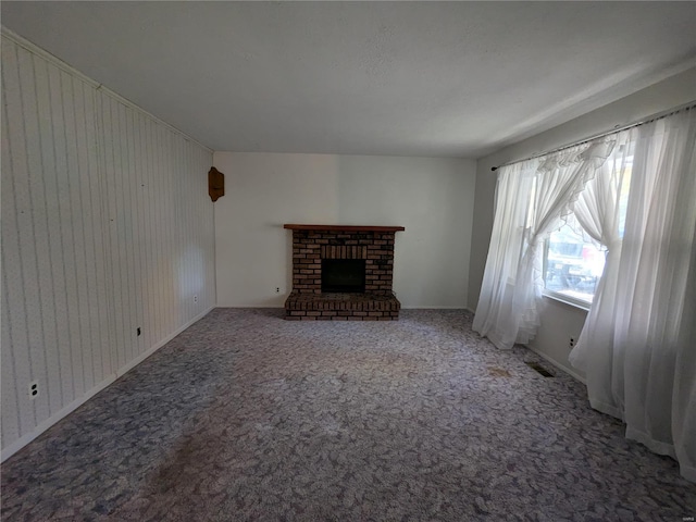 unfurnished living room with carpet, wooden walls, and a brick fireplace