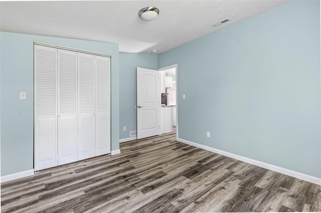 unfurnished bedroom with a textured ceiling, dark hardwood / wood-style floors, and a closet