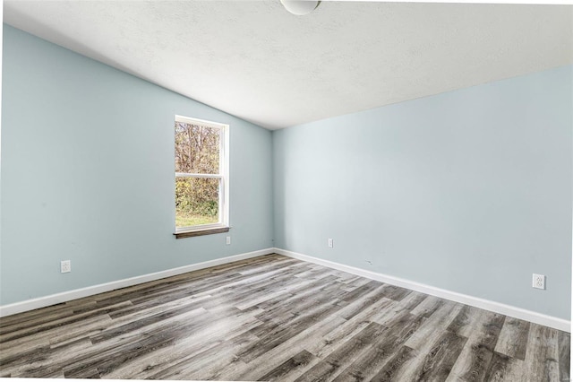 empty room with wood-type flooring, a textured ceiling, and vaulted ceiling