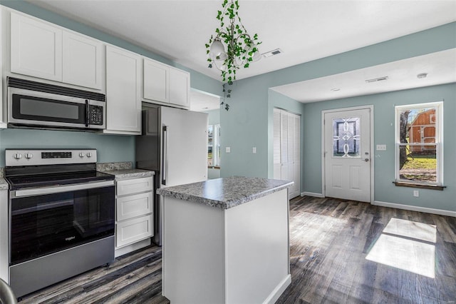 kitchen with white cabinets, dark hardwood / wood-style floors, appliances with stainless steel finishes, and a center island