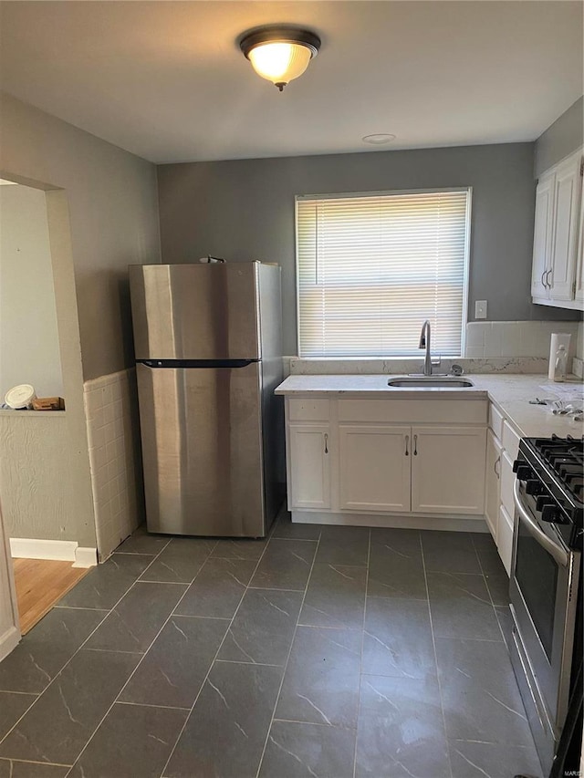 kitchen featuring stainless steel fridge, white cabinets, range with gas cooktop, dark tile patterned flooring, and sink