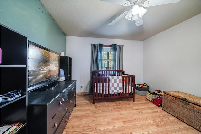 bedroom with a crib, ceiling fan, and light wood-type flooring