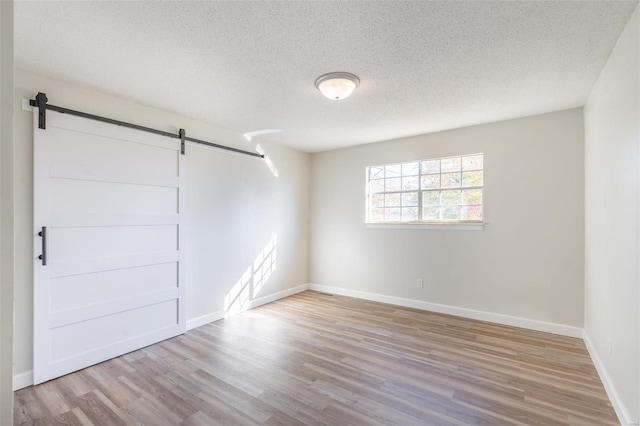 spare room featuring a barn door, a textured ceiling, and light hardwood / wood-style floors