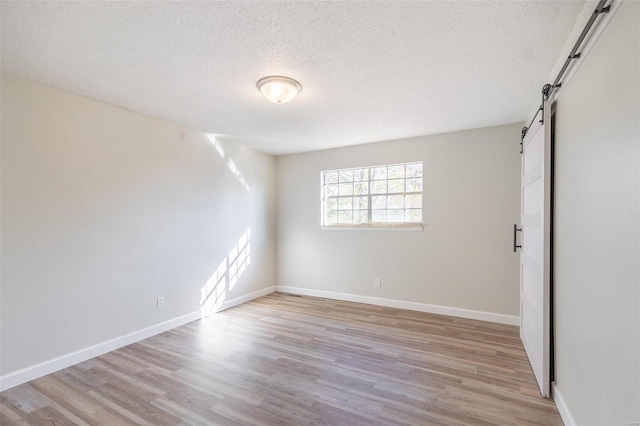 empty room featuring a textured ceiling, a barn door, and light wood-type flooring