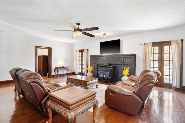 living room featuring french doors, a wood stove, wood-type flooring, and ceiling fan