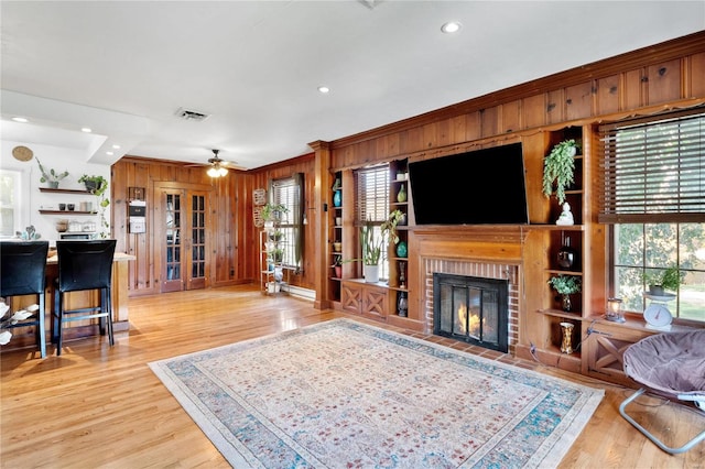 living room with a brick fireplace, ceiling fan, wooden walls, crown molding, and light hardwood / wood-style flooring