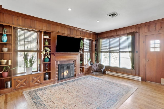 living room with plenty of natural light, wood walls, a baseboard radiator, and light wood-type flooring