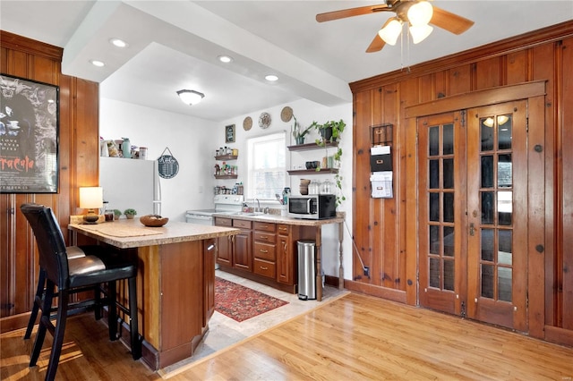 kitchen featuring kitchen peninsula, a kitchen breakfast bar, light hardwood / wood-style flooring, wood walls, and white appliances