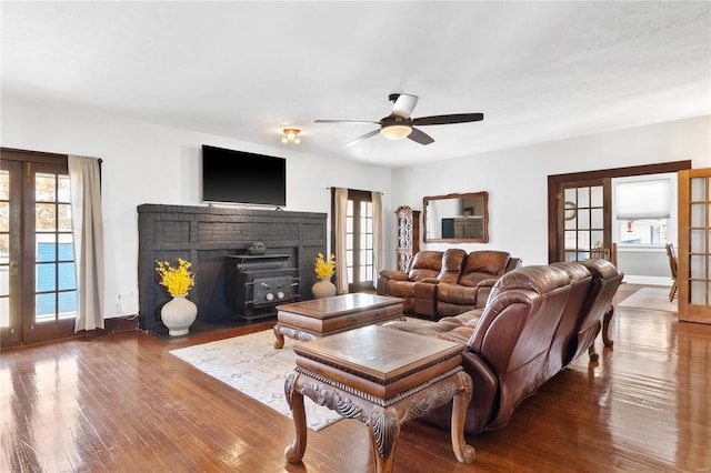 living room featuring french doors, ceiling fan, wood-type flooring, and a wood stove