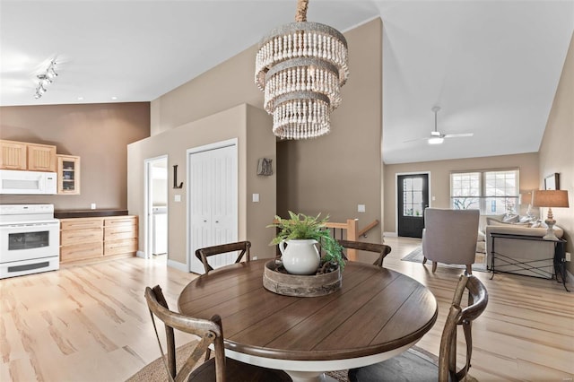 dining room with rail lighting, high vaulted ceiling, ceiling fan with notable chandelier, and light hardwood / wood-style floors