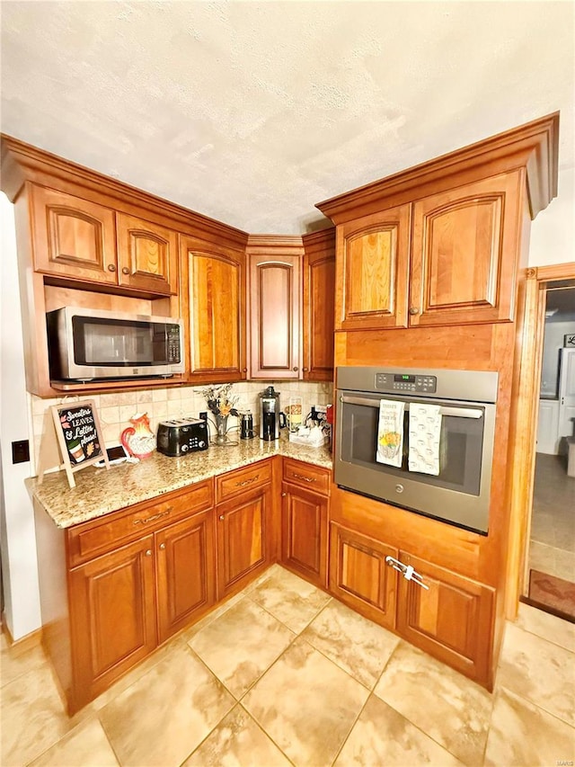 kitchen featuring a textured ceiling, stainless steel appliances, light stone counters, decorative backsplash, and light tile patterned floors