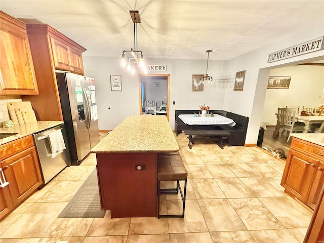 kitchen with light stone countertops, appliances with stainless steel finishes, a kitchen island, decorative light fixtures, and a breakfast bar