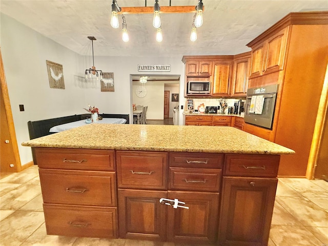 kitchen with a kitchen island, appliances with stainless steel finishes, light stone countertops, light tile patterned flooring, and decorative light fixtures